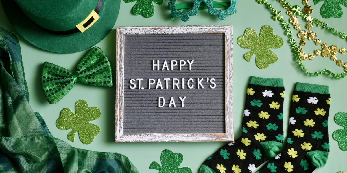 Green-themed St. Patrick's Day items surround a letter board reading "Happy St. Patrick’s Day." Includes a leprechaun hat, bow tie, shamrocks, and socks.