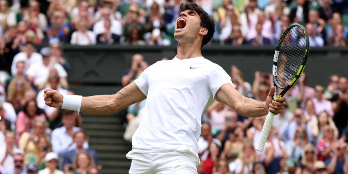 Tennis player in white celebrates with a loud yell, clenching fists and holding a racket, in front of a cheering crowd. The scene conveys triumph and excitement.