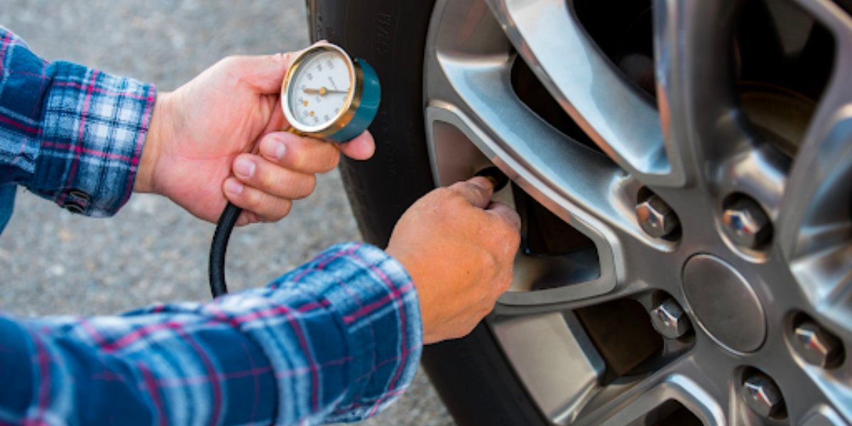 A person in a plaid shirt checks a car tire's pressure using a gauge. The focus is on the tire and gauge, emphasizing maintenance and care.